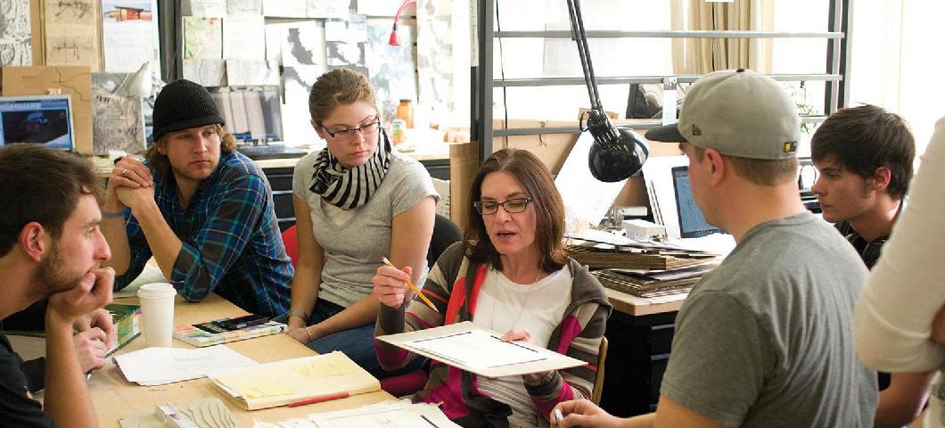 Three architecture students examine drawings of building designs.