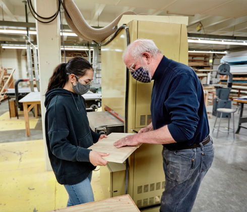 Student Stephanie Weddle inspects a wood panel with Bill Clinton, fabrication shop director.